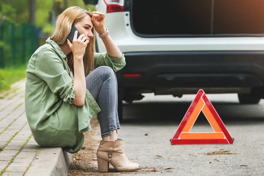 Frau sitzt am Straßenrand vor ihrem Pannenfahrzeug und telefoniert